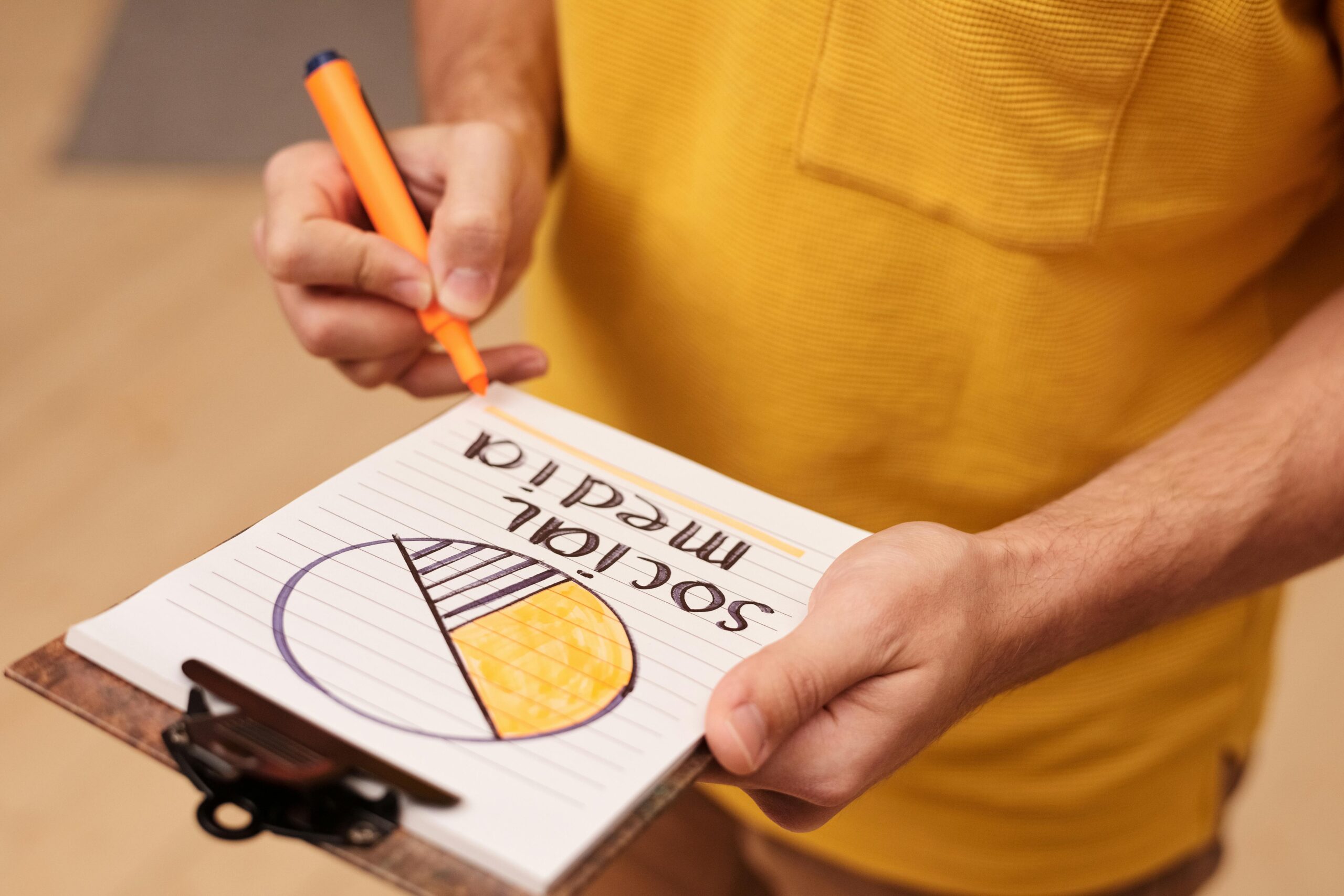 Person draws a social media pie chart on clipboard with orange marker.
