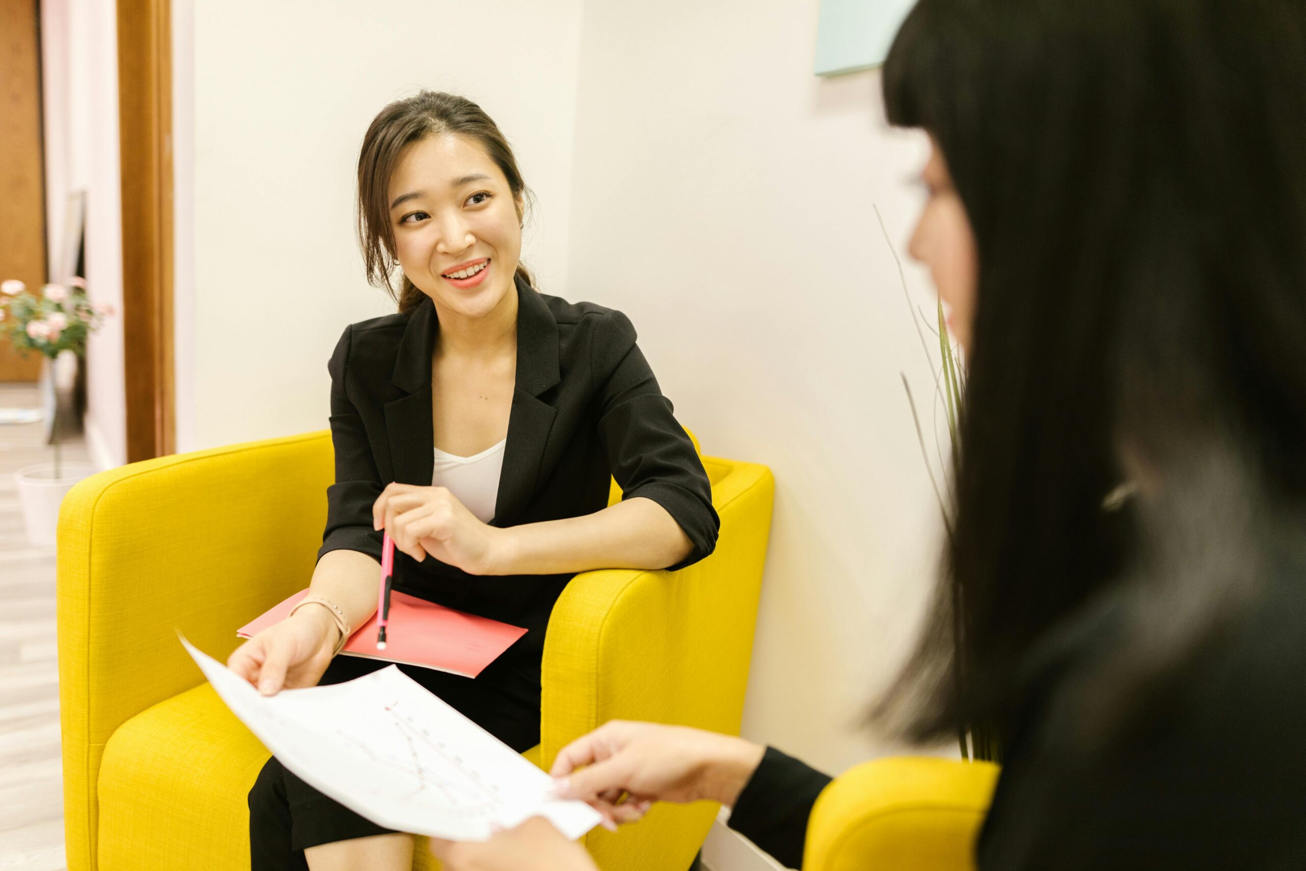 Two professional women having a discussion in an office with documents in hand.
